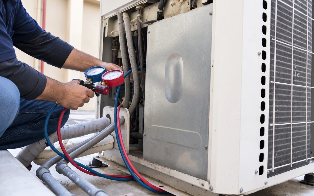 SquareHVAC technician checking a commercial split-system condenser with analog manifold gauges