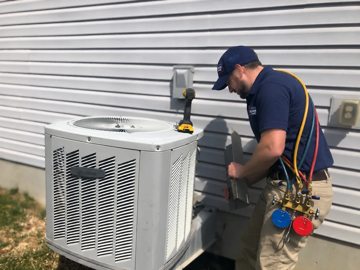 SquareHVAC technician connecting manifold gauges to a Trane condenser during residential air-conditioning installation